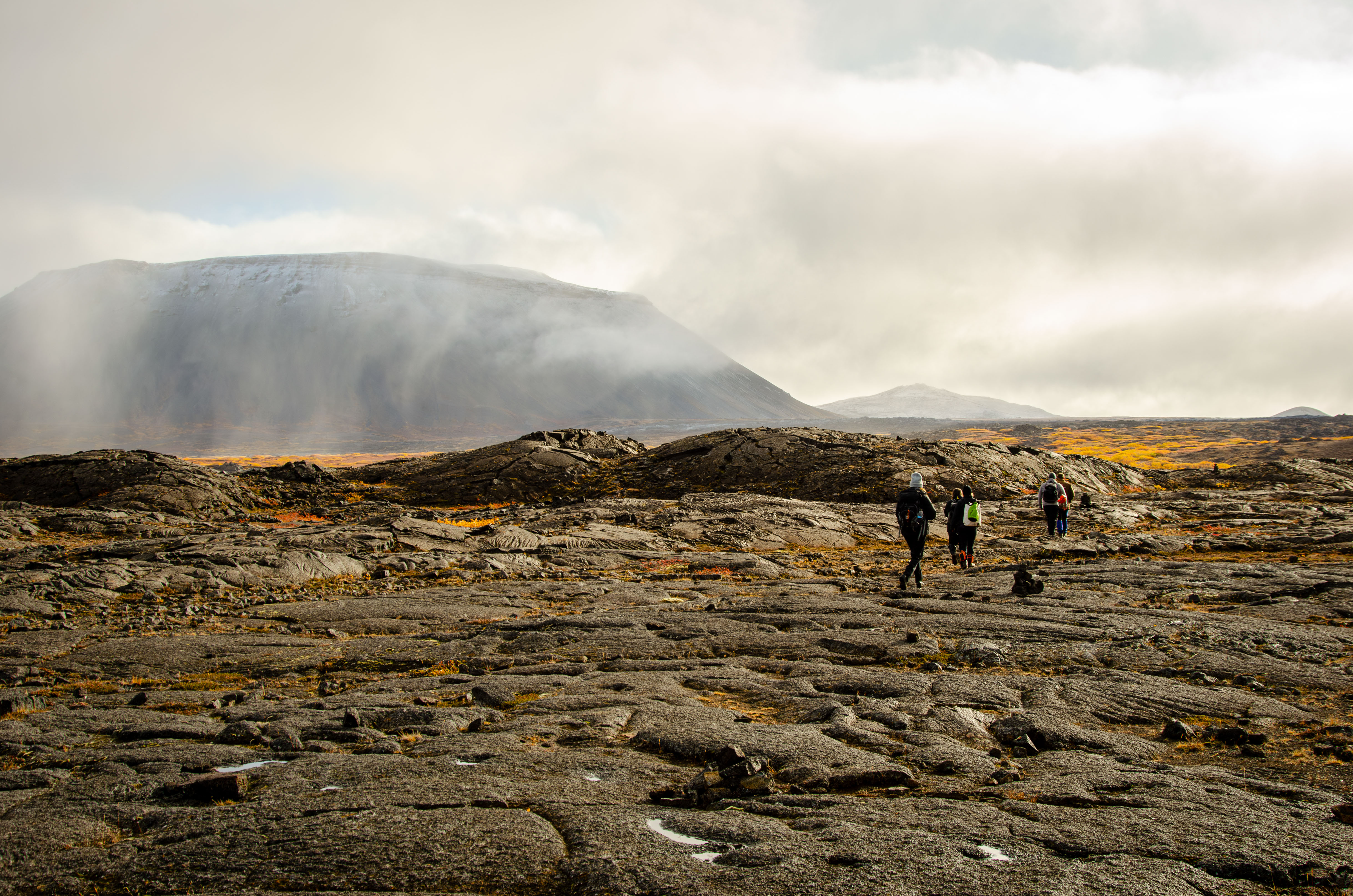 Team traversing Icelandic volcanic landscape toward fog-covered mountain
